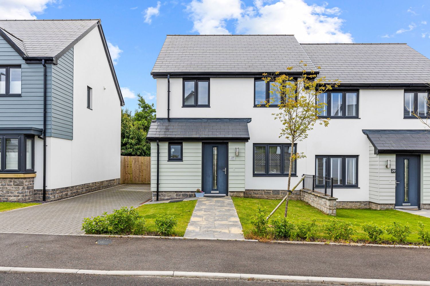 Modern two-story townhouse with grey exterior, black windows, and paved driveway in new development.