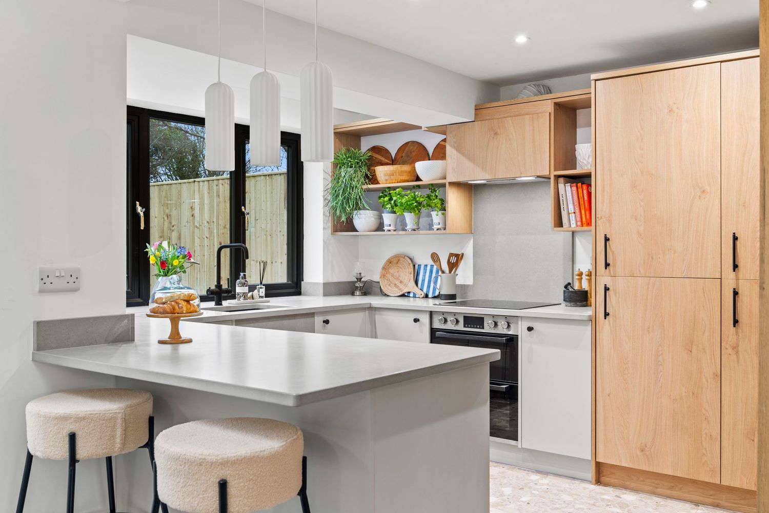 Modern kitchen with light wood cabinets, white countertops, and a minimalist breakfast bar with two stools.