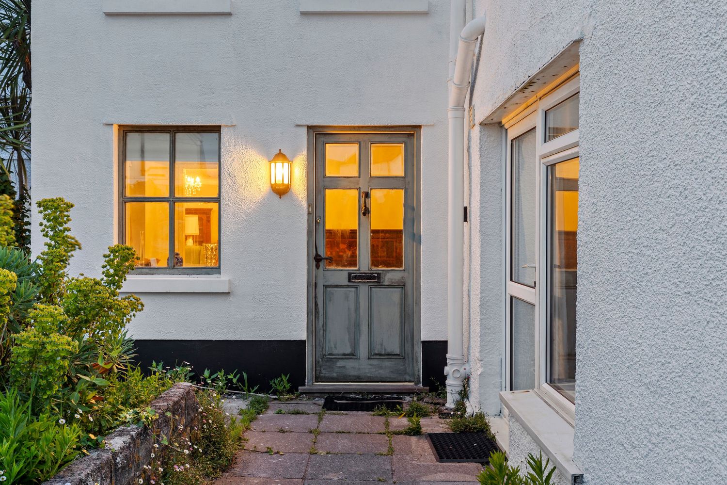 Illuminated front door and windows of a white stucco house at dusk with warm glowing interior lights.