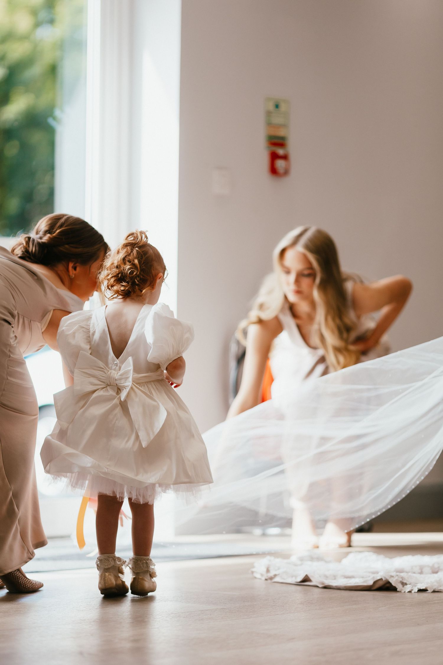 Sweet moment with little girl in white dress being helped with her bow while bride adjusts her gown.