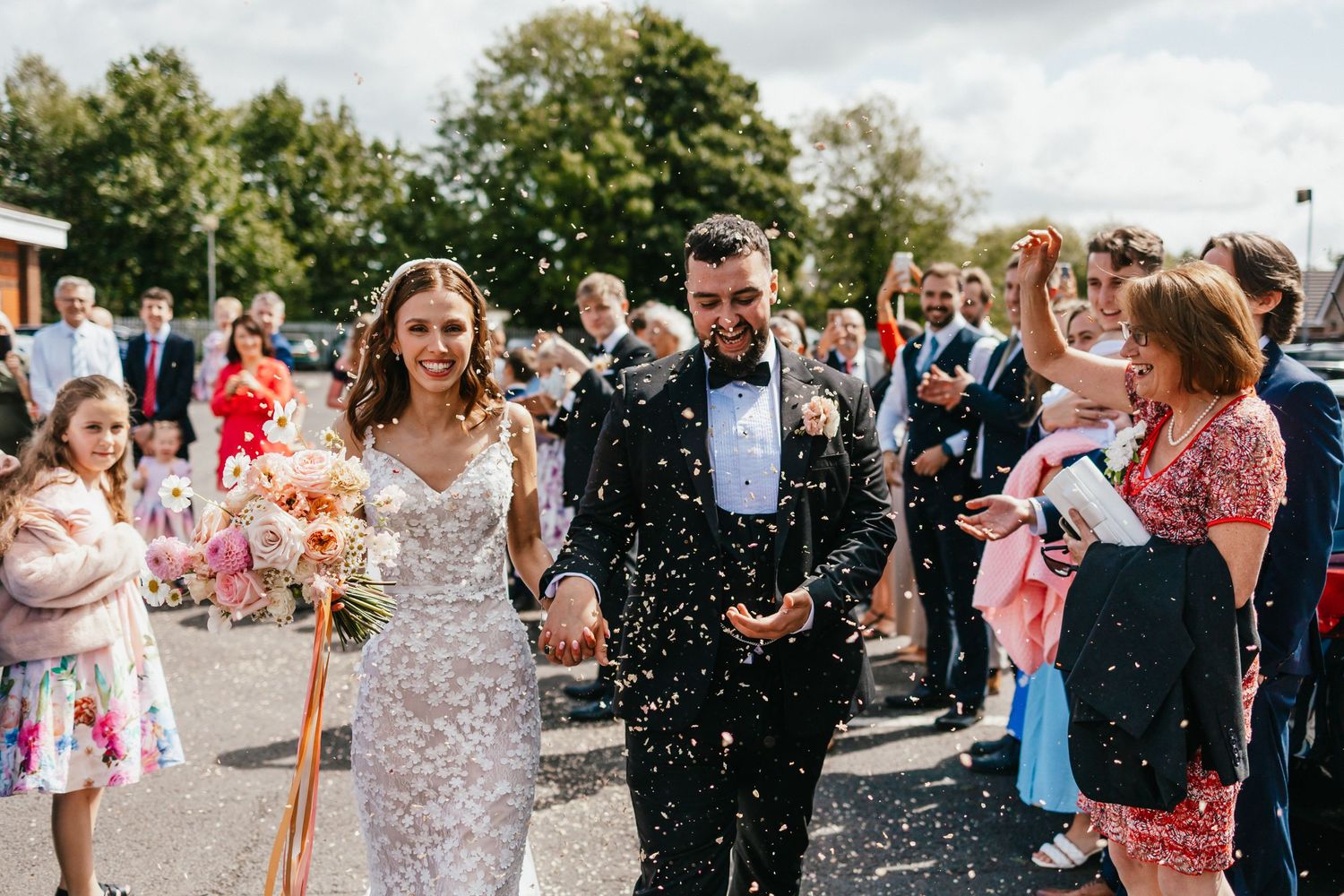 Newlyweds walk through confetti shower surrounded by cheering wedding guests.
