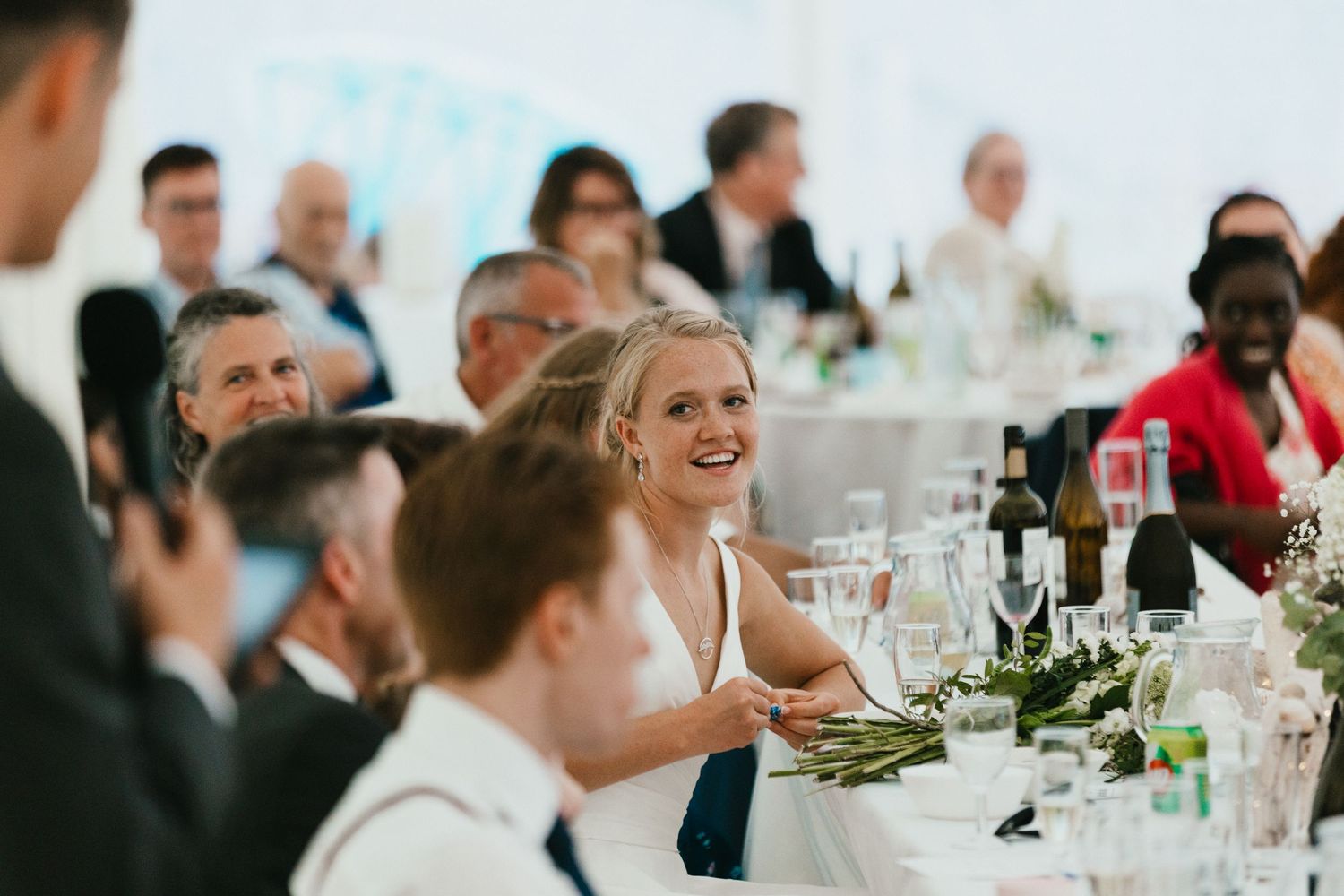 Wedding guests enjoying a reception dinner with wine glasses and table decorations at an elegant venue.