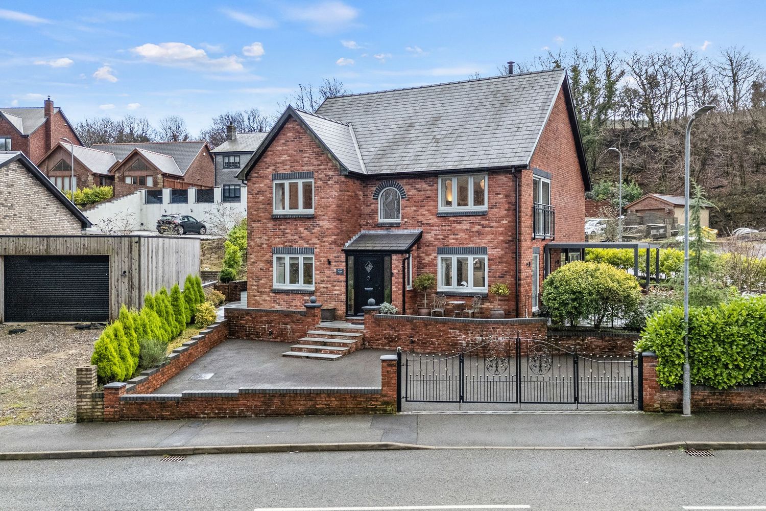 Traditional red brick detached house with manicured front garden and decorative iron gates.