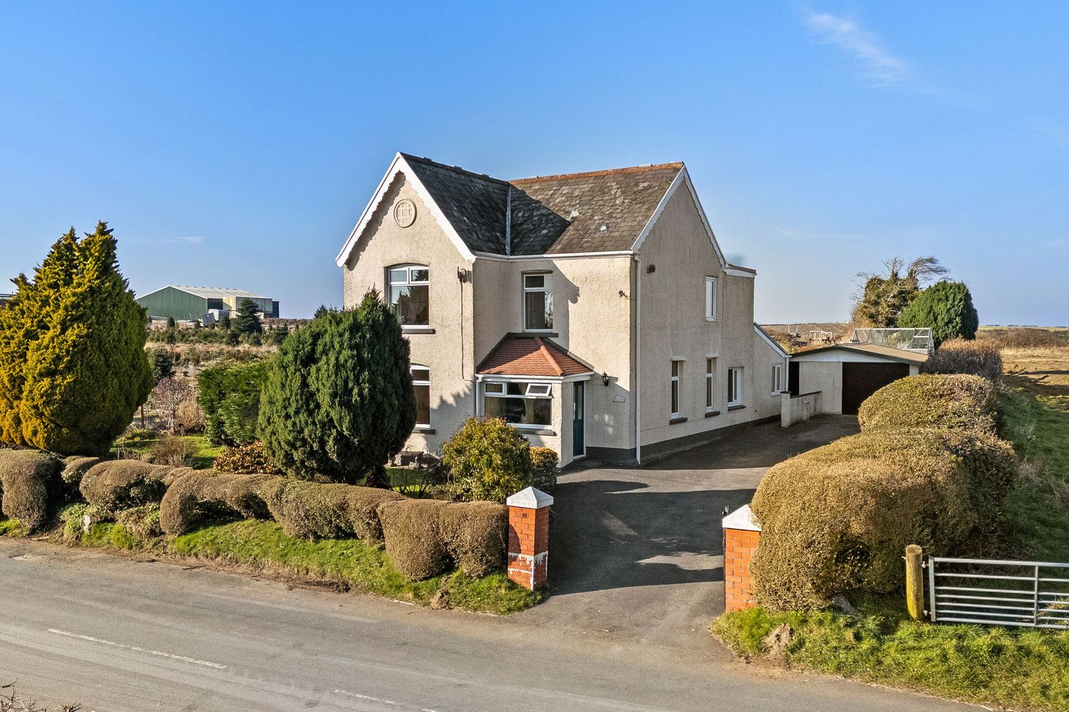 Detached cream colored house on elevated position with private driveway and surrounding greenery.