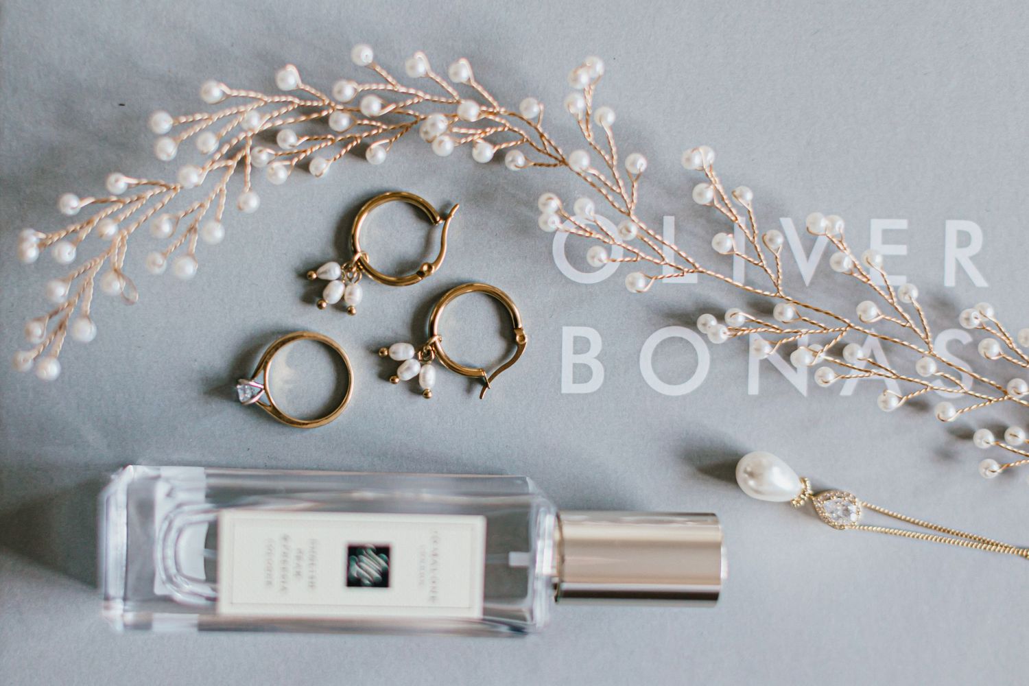 Wedding accessories including pearl vine, rings and perfume bottle arranged on gray surface.
