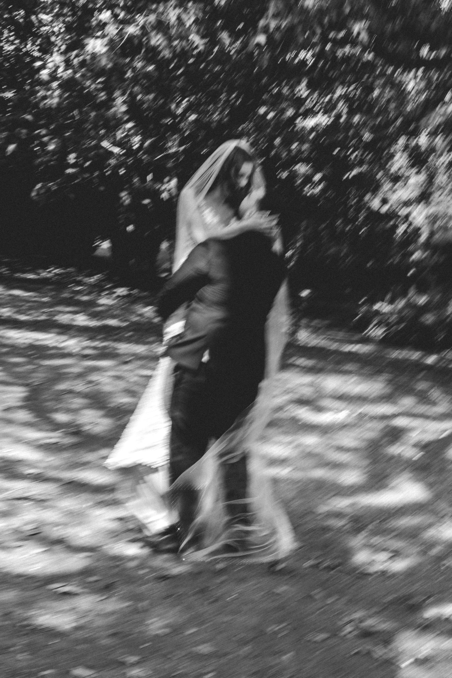 A blurred black and white artistic wedding photo showing a couple dancing outdoors among trees.