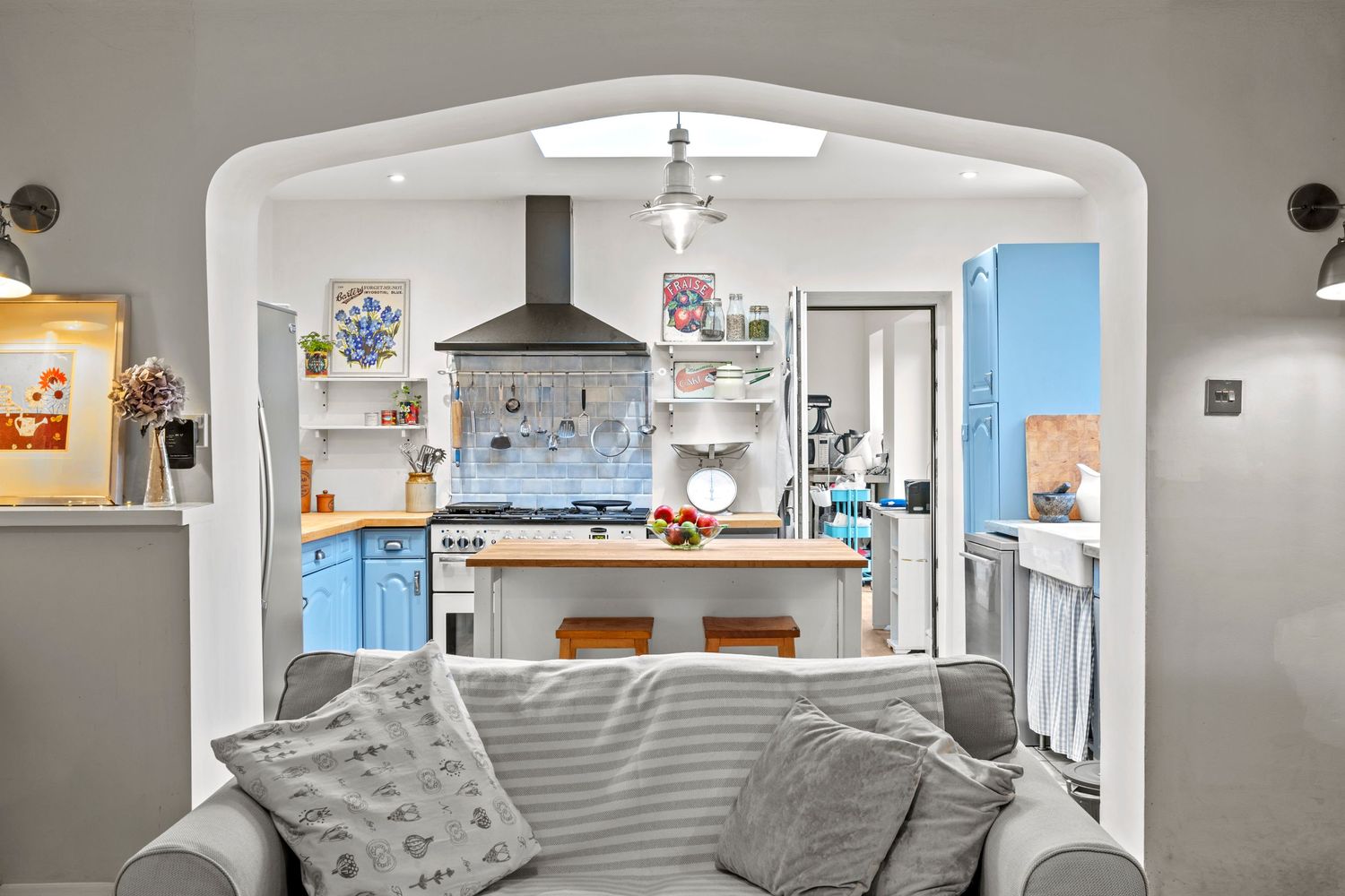 Cozy living room view through archway to bright kitchen with blue accents and central island.
