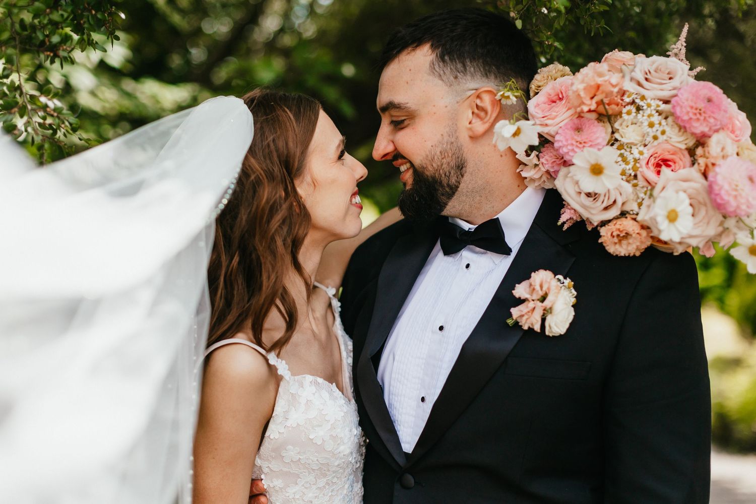 Wedding couple sharing an intimate moment among pink floral bouquets in a garden setting.
