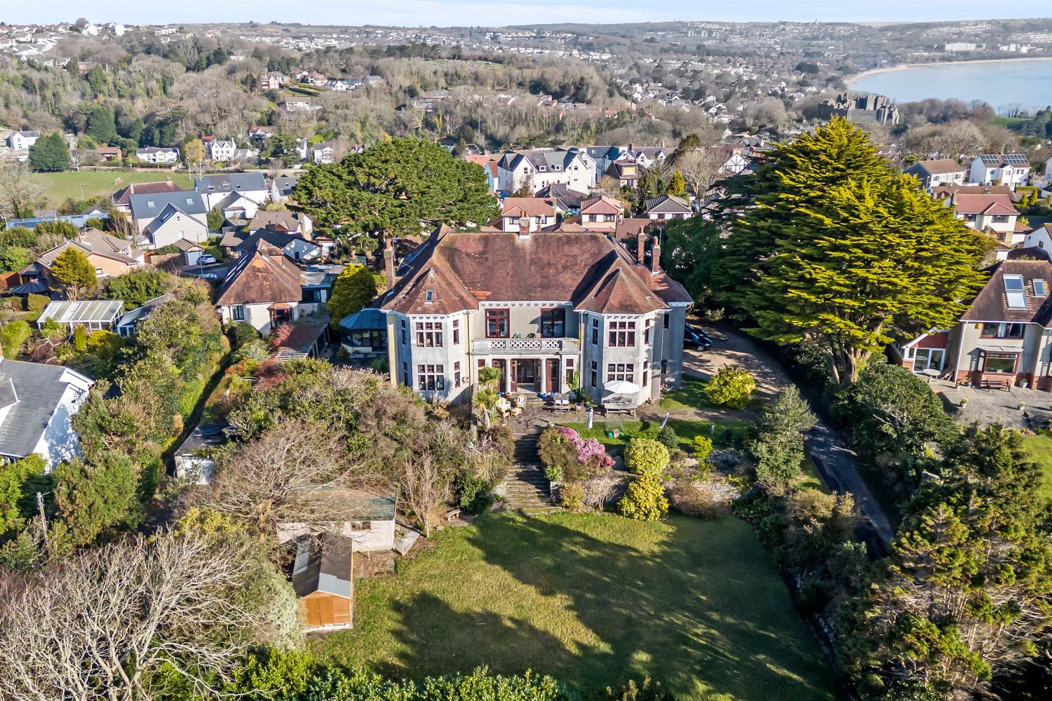 Aerial view of a large Victorian mansion with extensive gardens overlooking a coastal town.