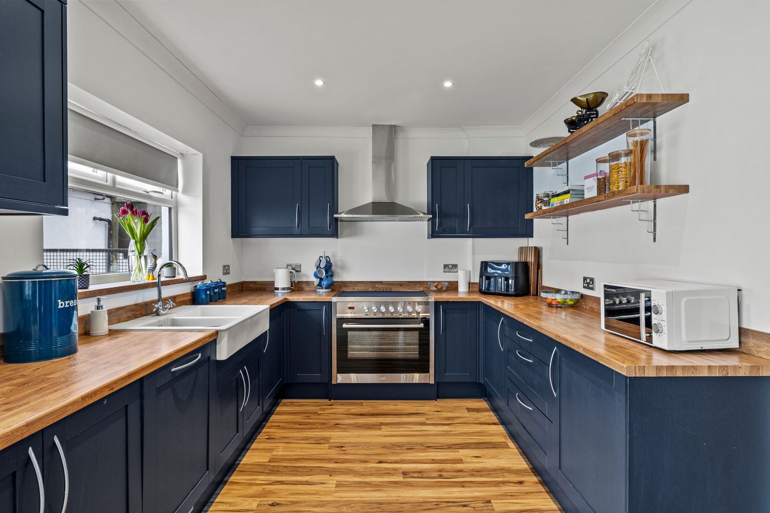 Navy blue kitchen with wooden countertops and stainless steel appliances.