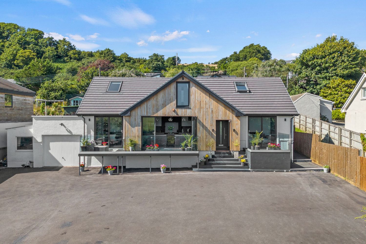 Contemporary grey and wood-clad house with large windows and spacious driveway in hillside setting.