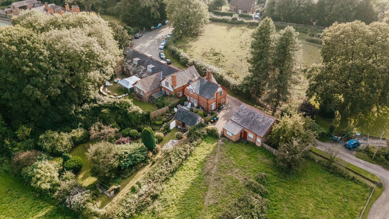 Aerial view of rural English countryside houses with gardens and winding road.
