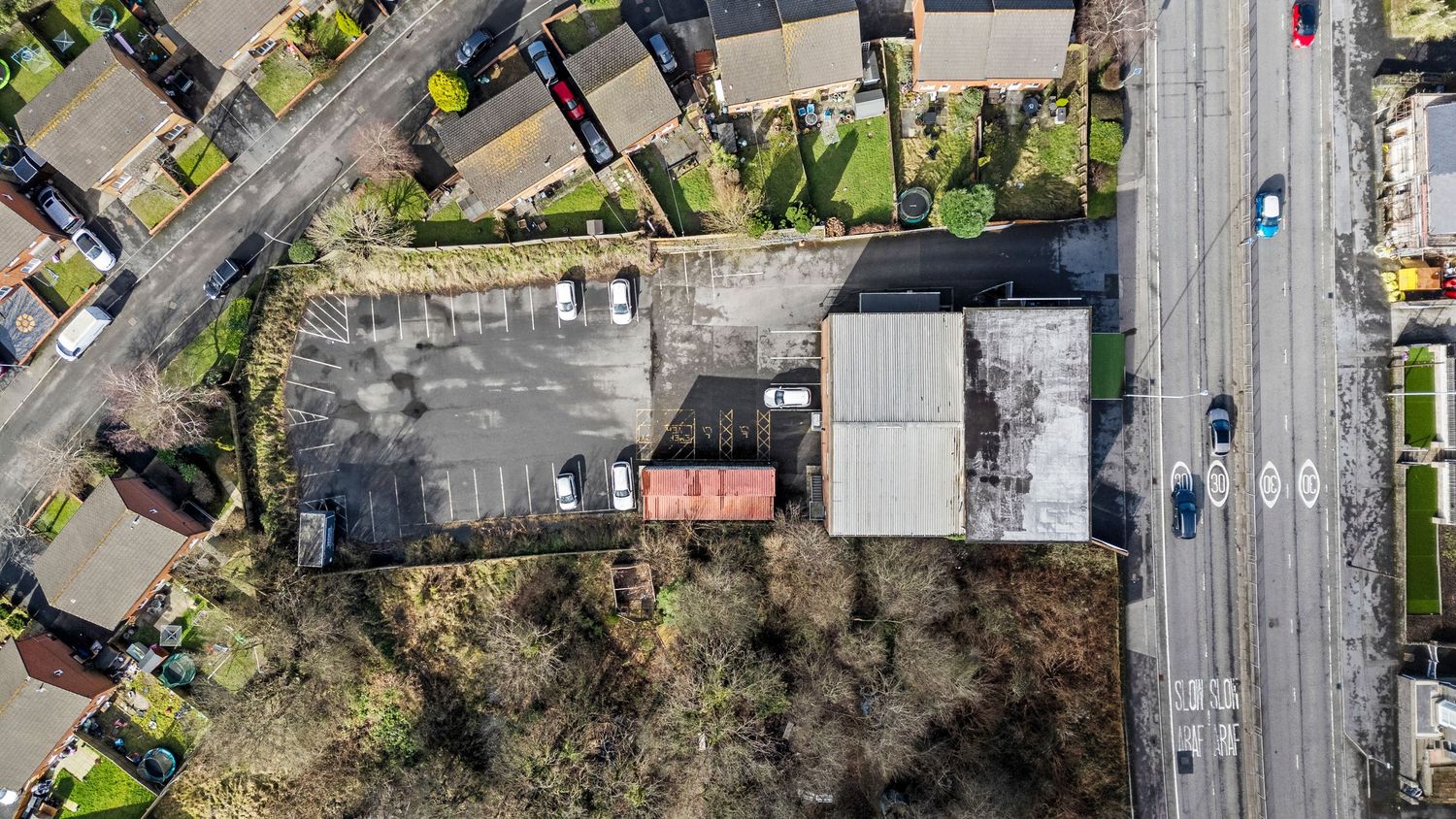 Aerial view of a commercial property with parking lot and warehouses adjacent to a main road.