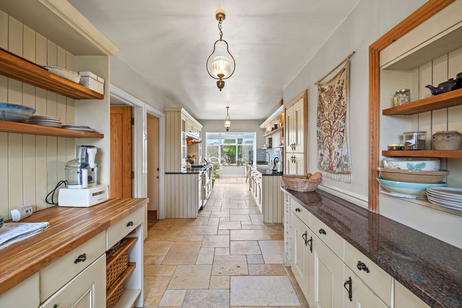 Long galley kitchen with wooden countertops, cream cabinets and traditional pendant lighting.