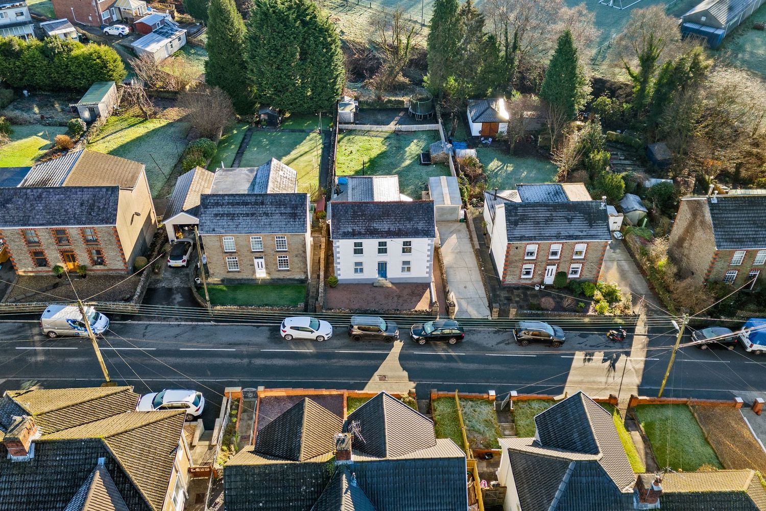 Drone shot of terraced houses along a suburban street with front gardens and driveways.