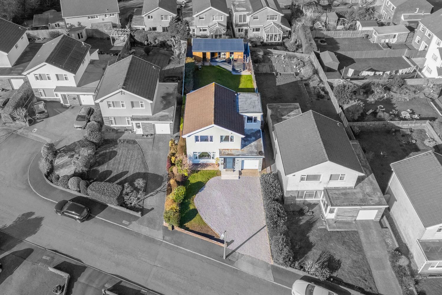 Color-highlighted modern home amidst black and white aerial view of suburban neighborhood.