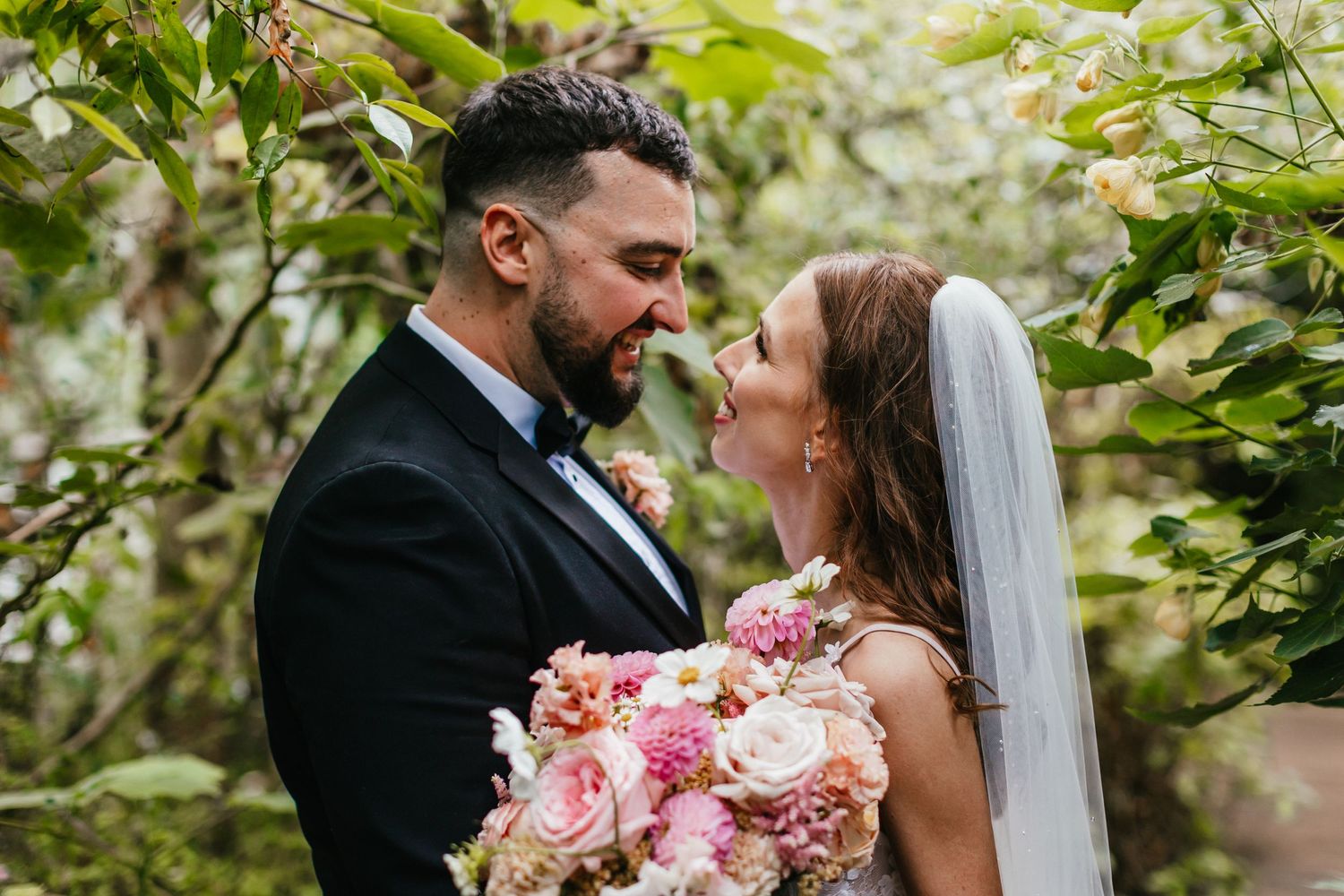A loving moment captured in a garden setting with pink floral bouquet.
