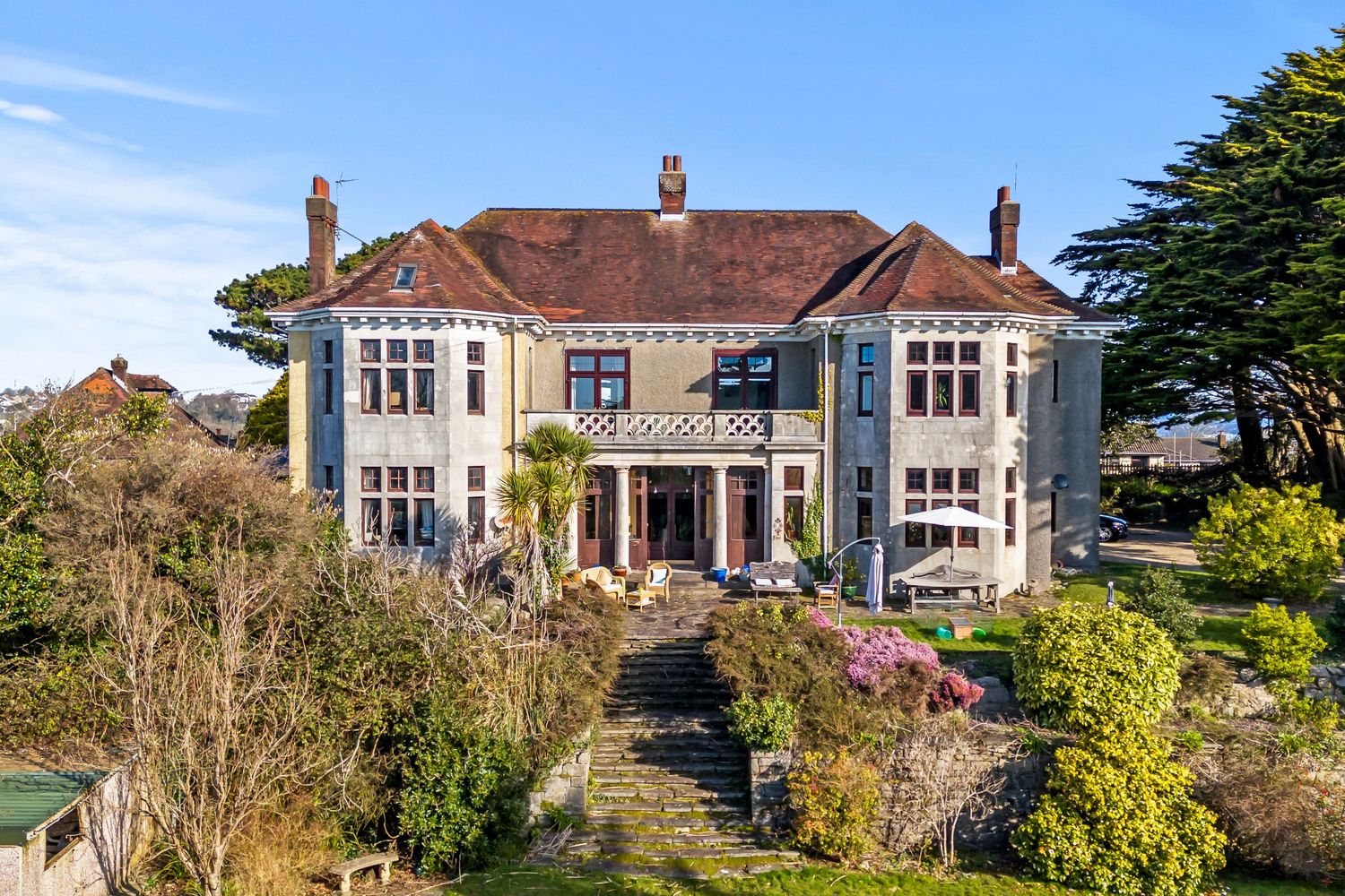 Grand period property with bay windows and manicured gardens overlooking coastal views.