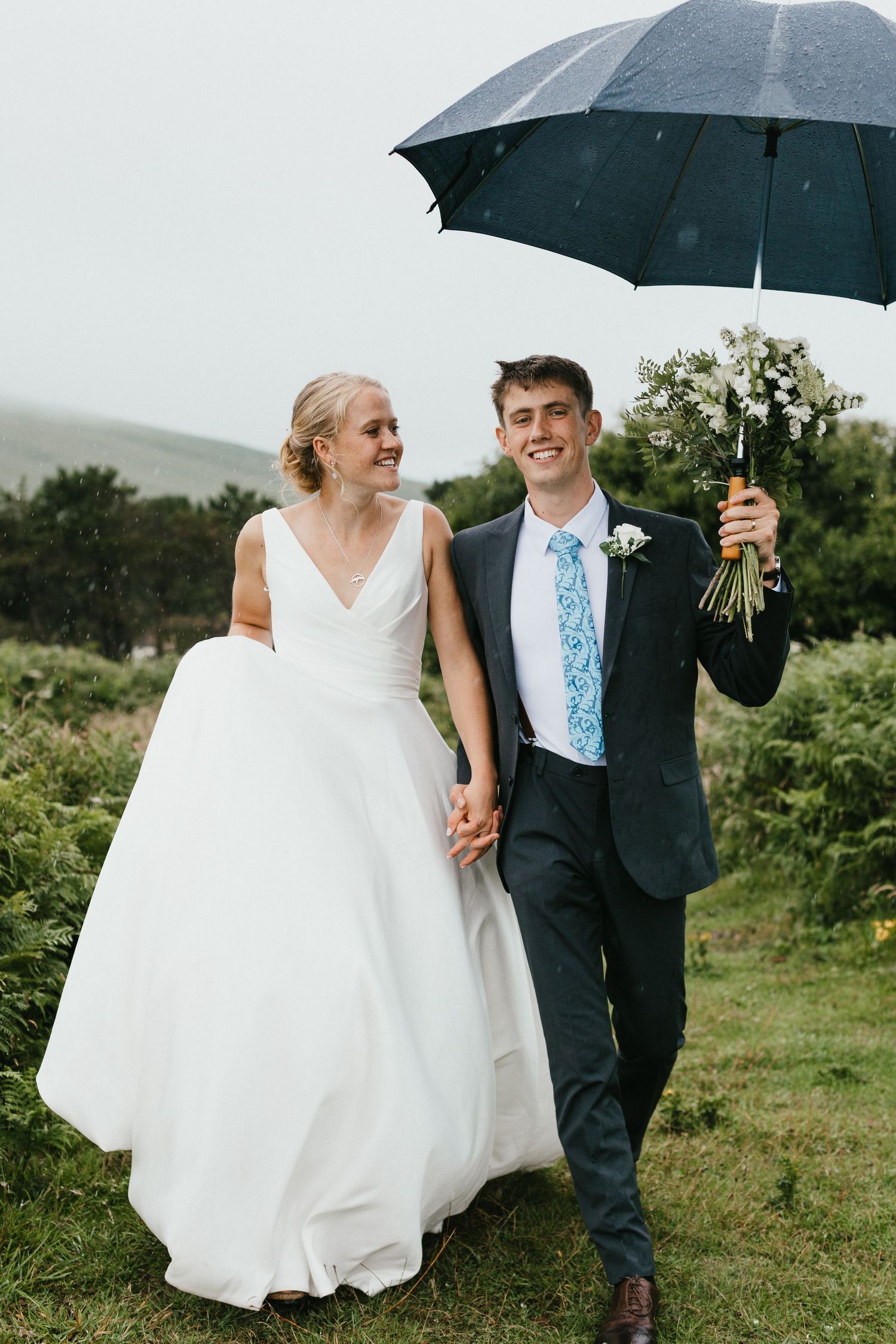 A wedding couple shares a moment under a black umbrella on an overcast day.