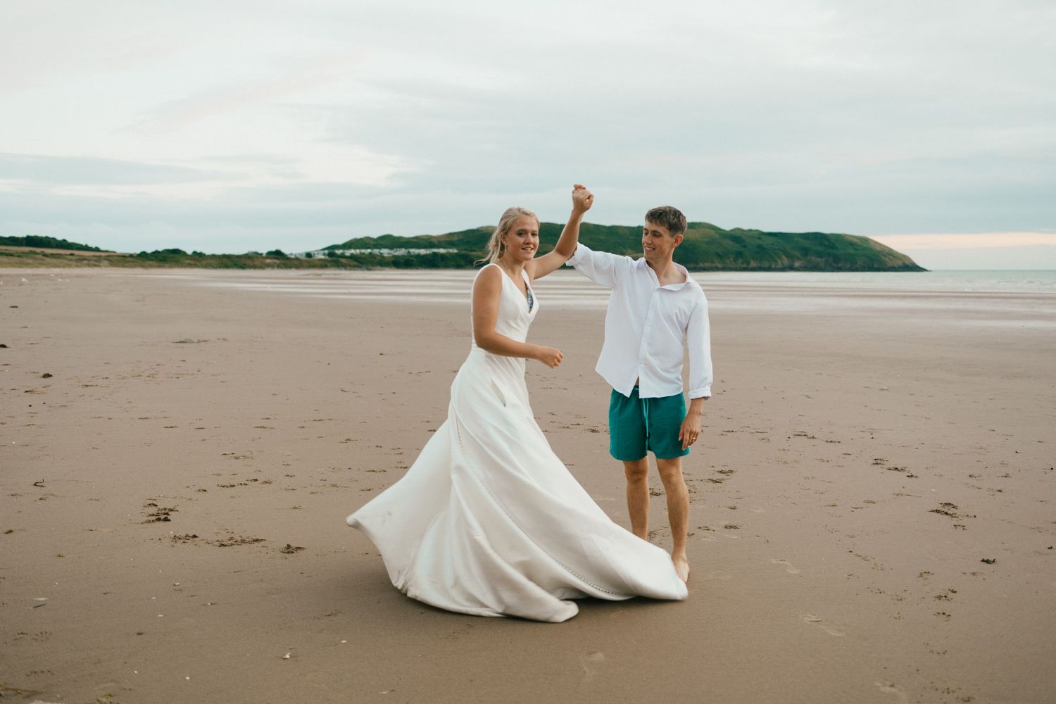 Couple in wedding attire share a joyful moment on a sandy beach.