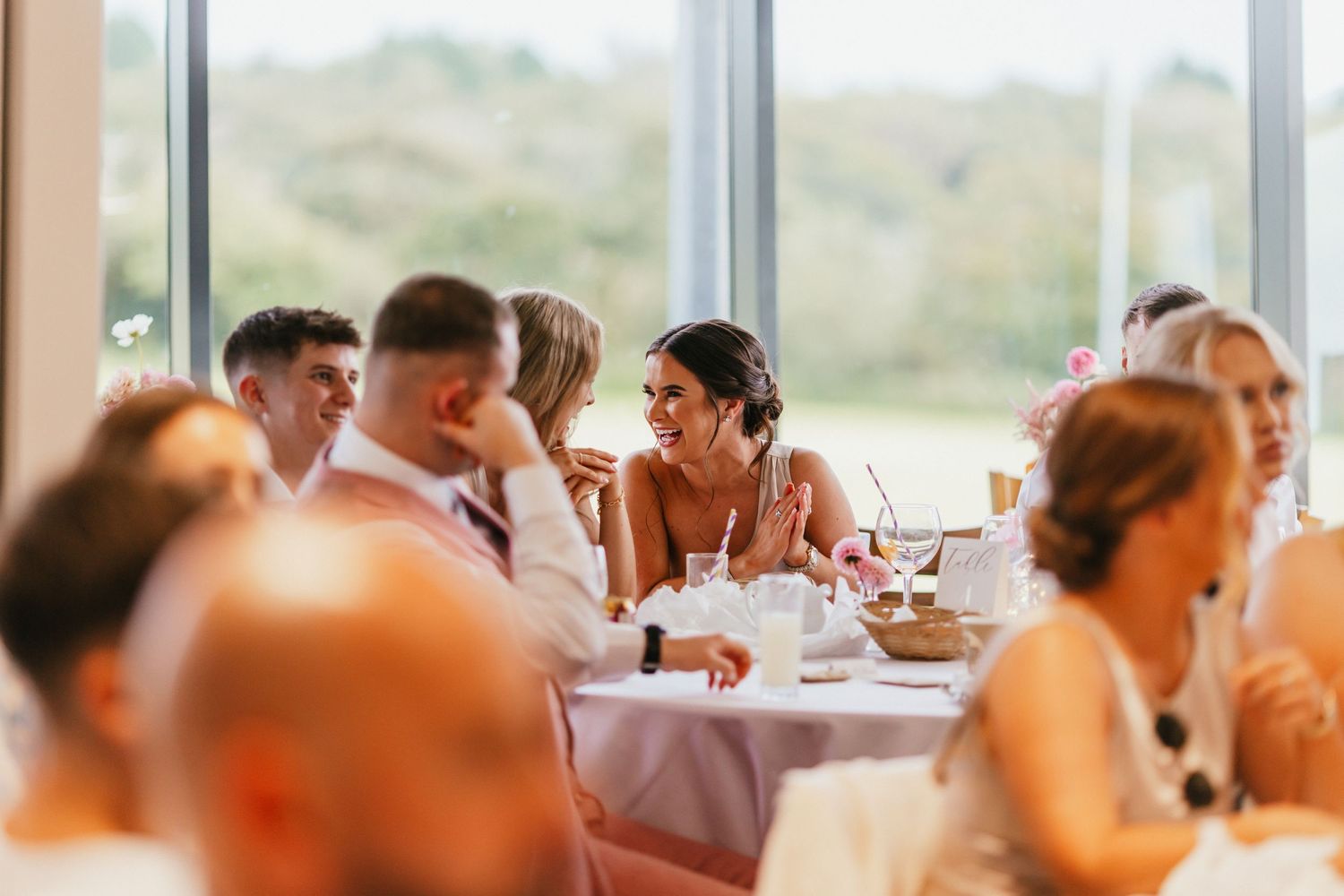Natural light streams through windows as wedding guests dine and converse at reception tables.