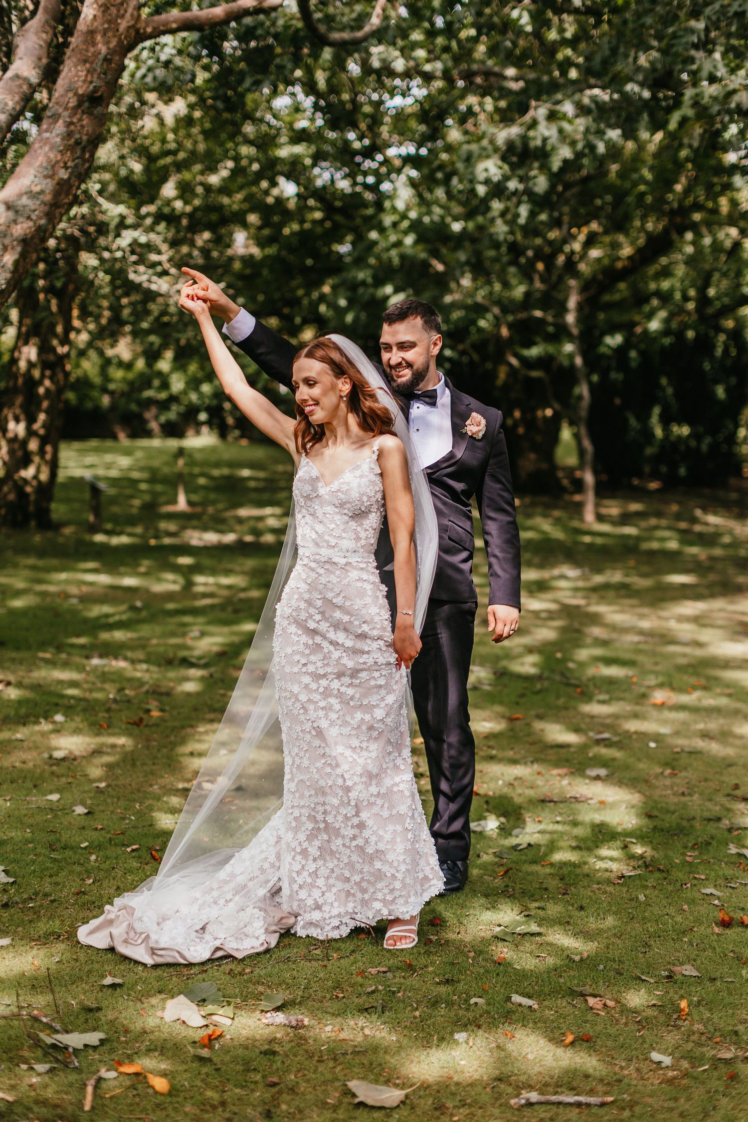 Joyful wedding dance moment on a sunlit lawn with flowing lace dress.