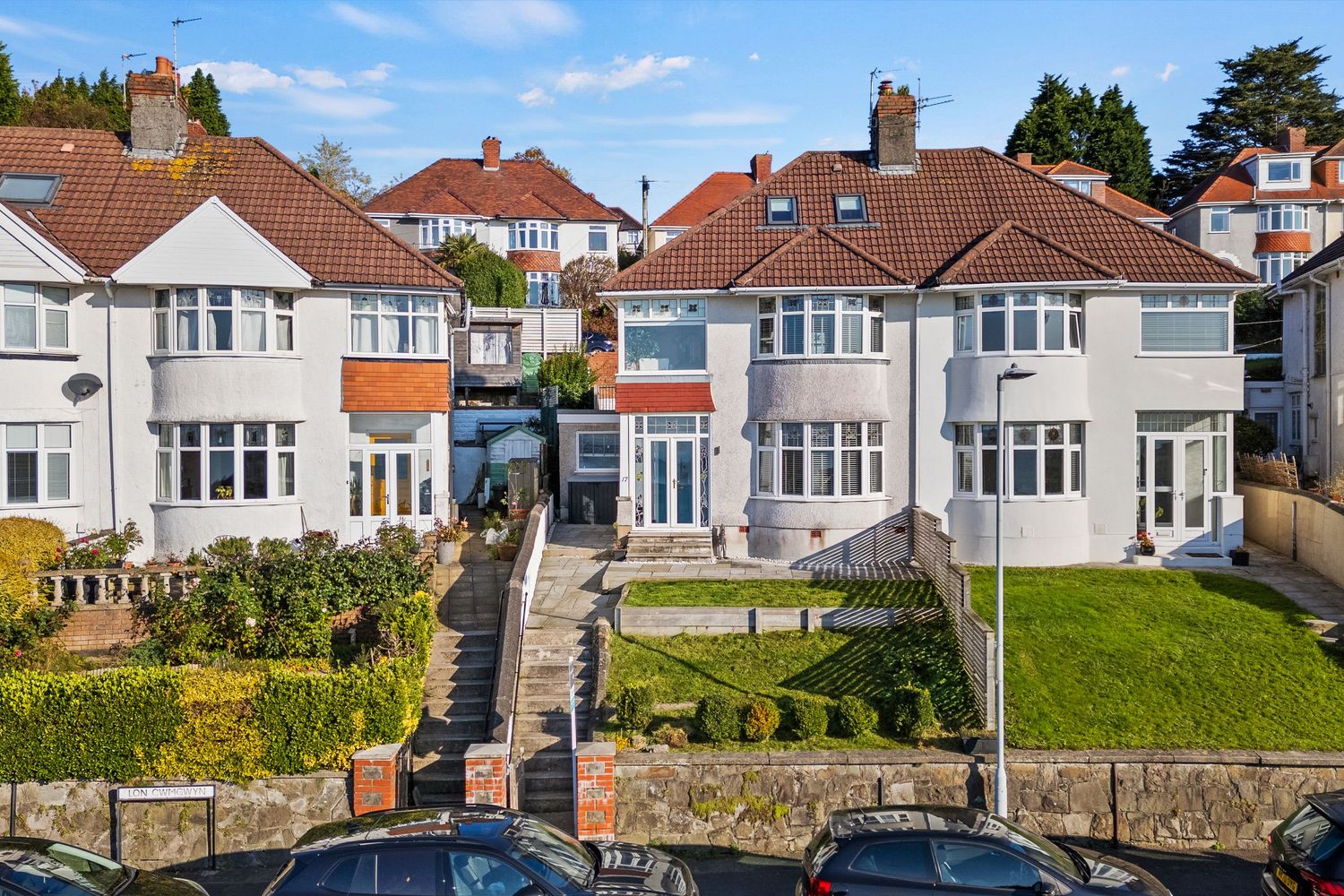 Row of large semi-detached houses with stepped gardens on a hillside overlooking the street.