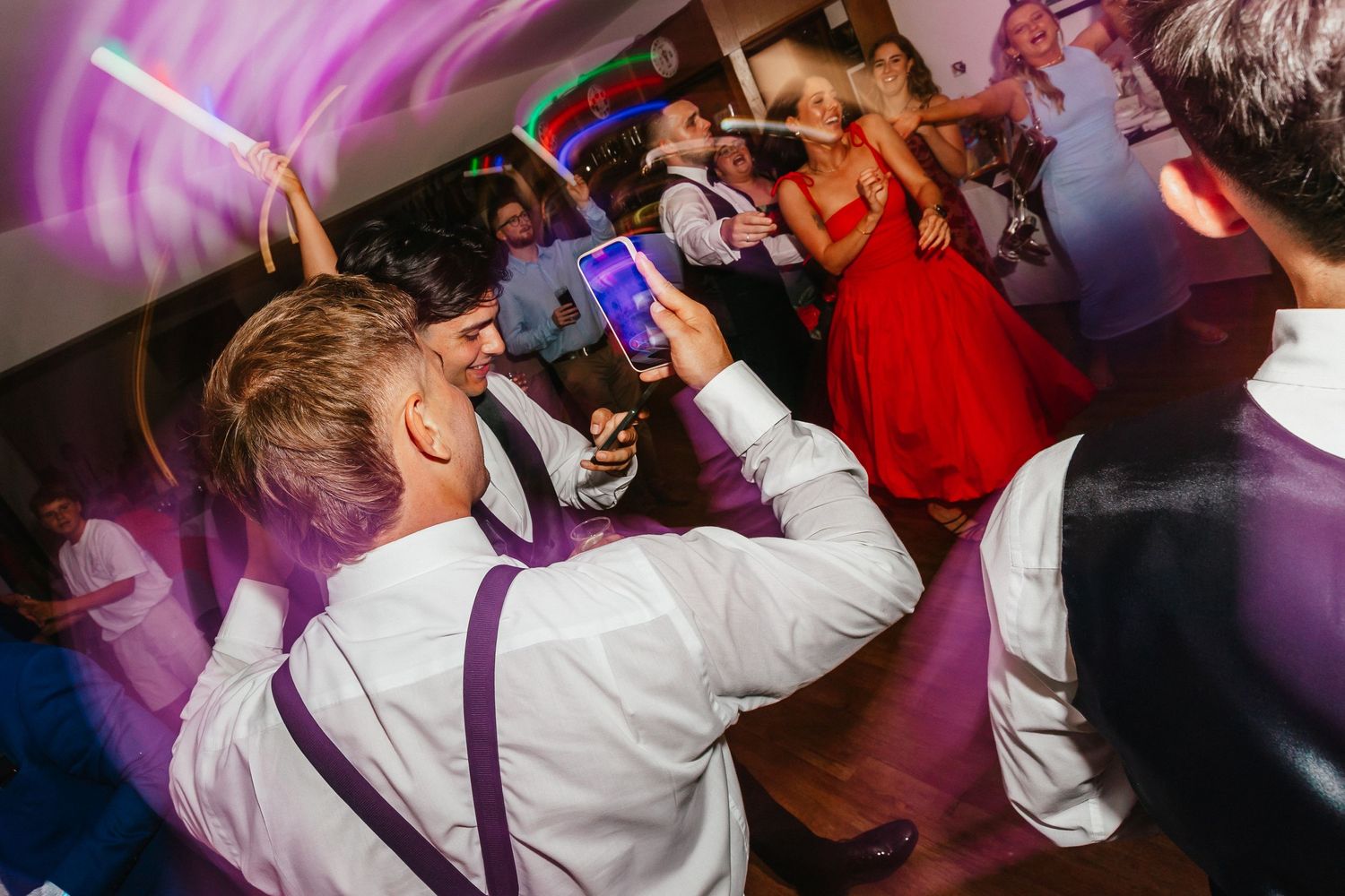 Guest in suspenders celebrates on the dance floor with colorful lights overhead.