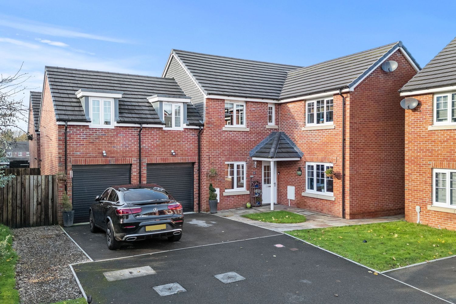 Large modern red brick house with double garage and landscaped front garden.