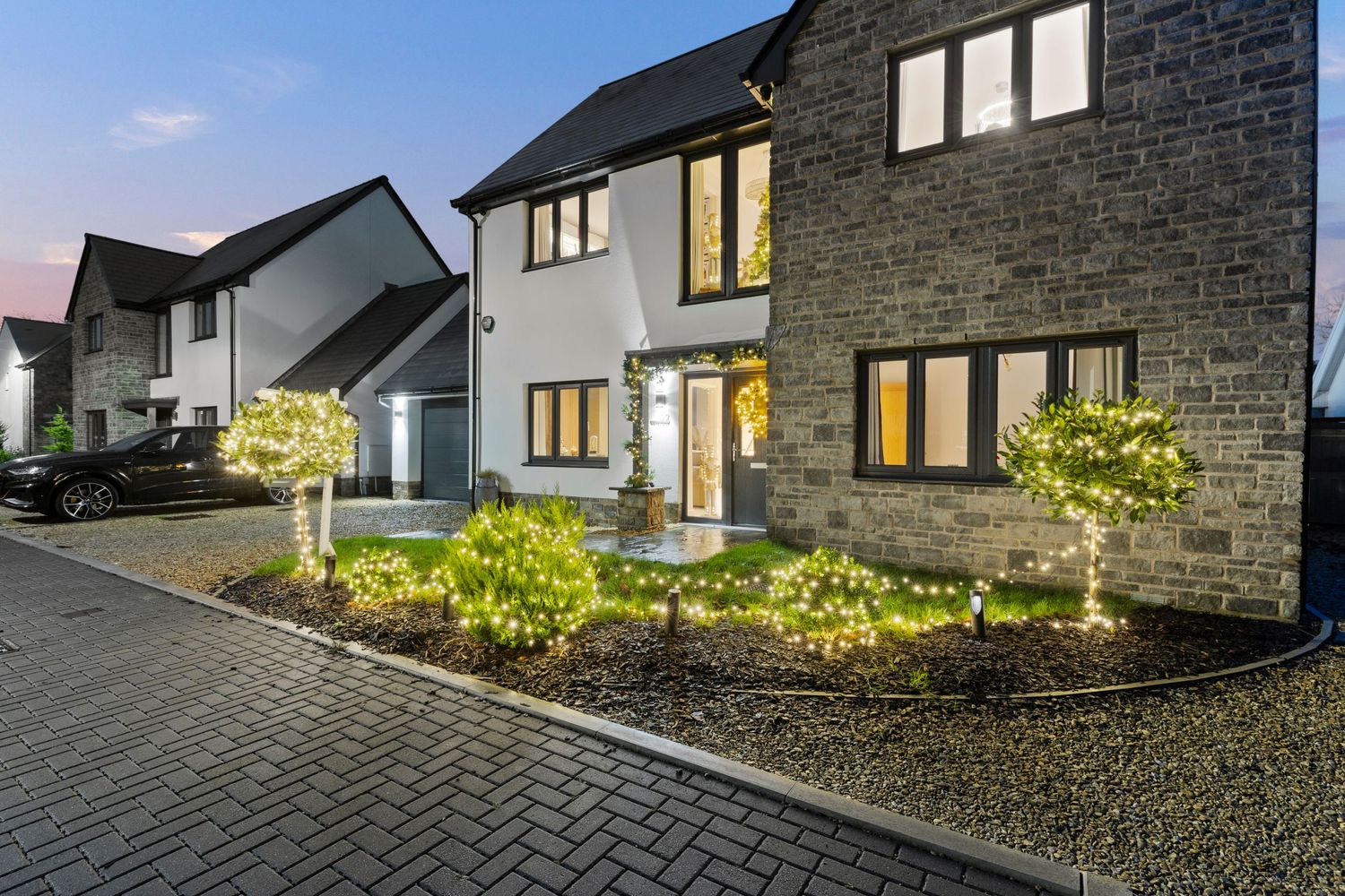 Modern stone house exterior with landscaped garden lights and paved driveway at dusk.