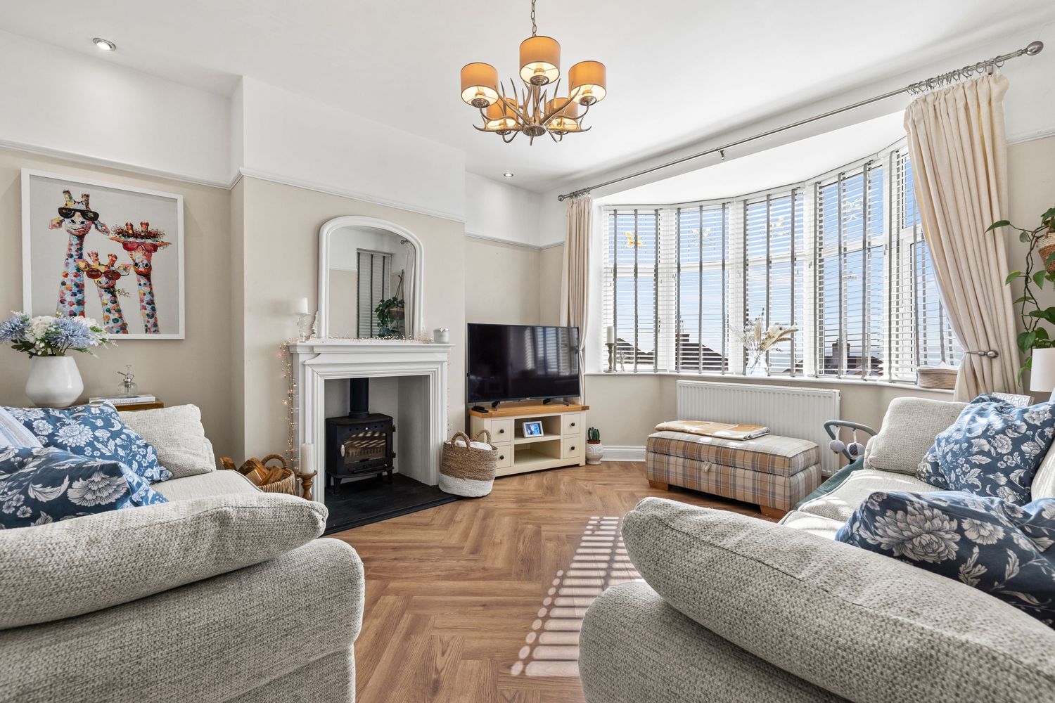 Elegant living room with bay window, fireplace, and grey sofas featuring herringbone wooden flooring.