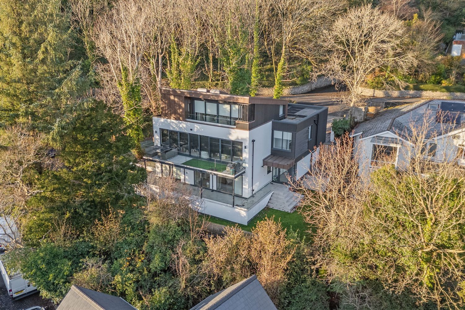 Modern multi-level house with glass walls nestled among trees, captured in aerial view.