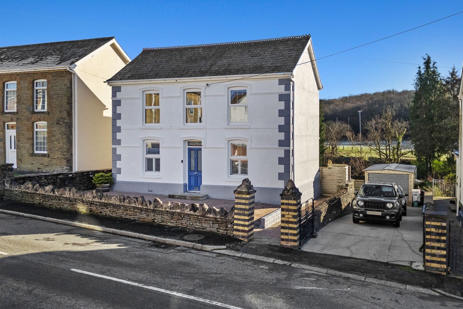 White painted traditional house with blue door and stone wall facade on a residential street.