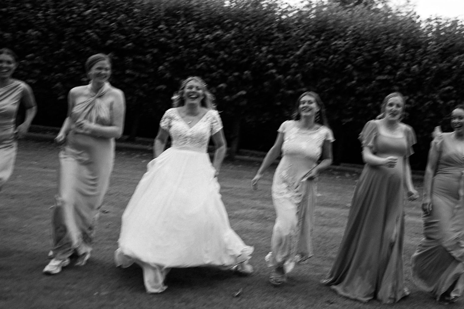 Black and white photo of wedding party running in sync on grass.