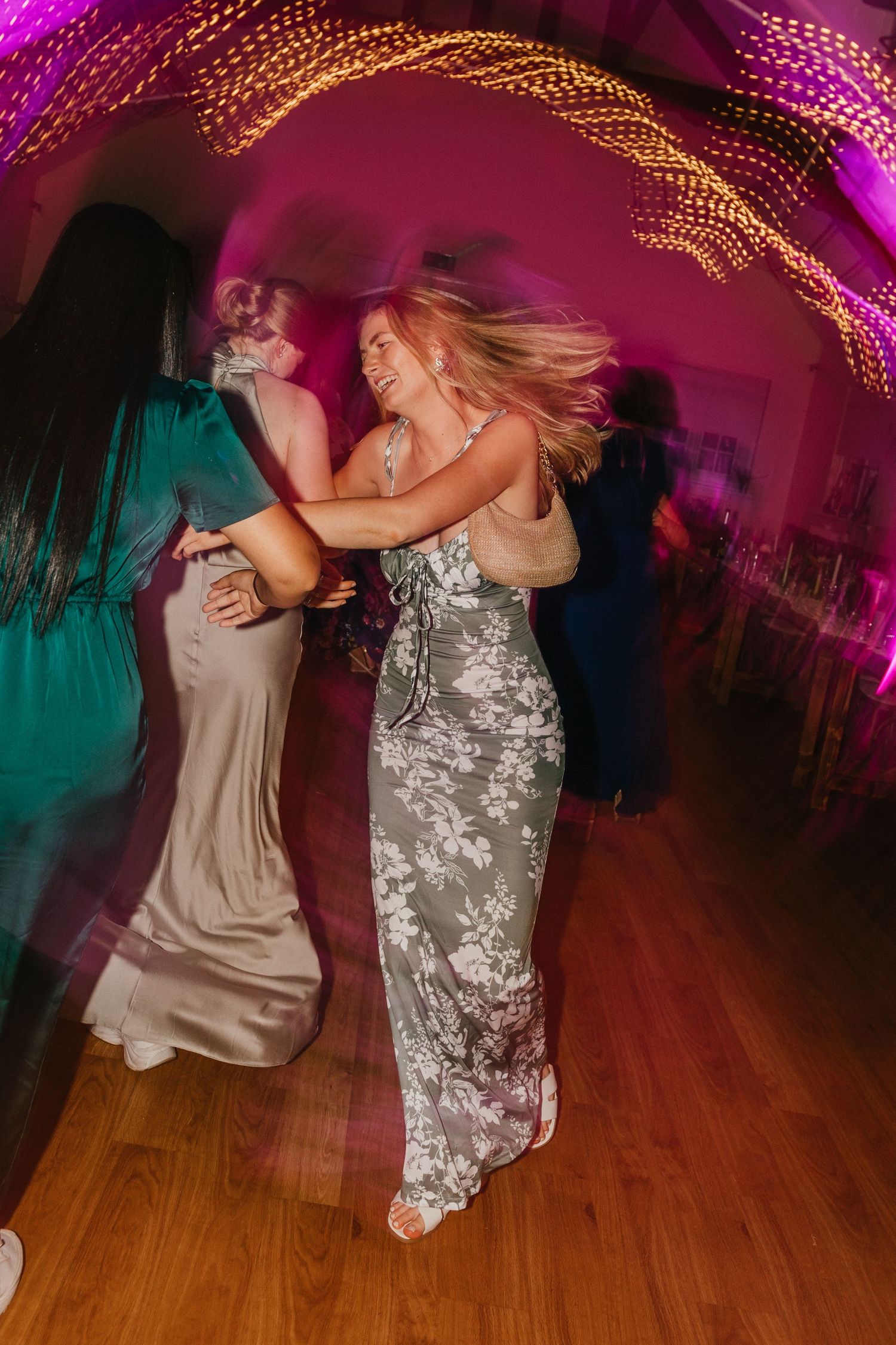 Wedding guests dancing energetically under purple lighting with a sparkly dress in motion.