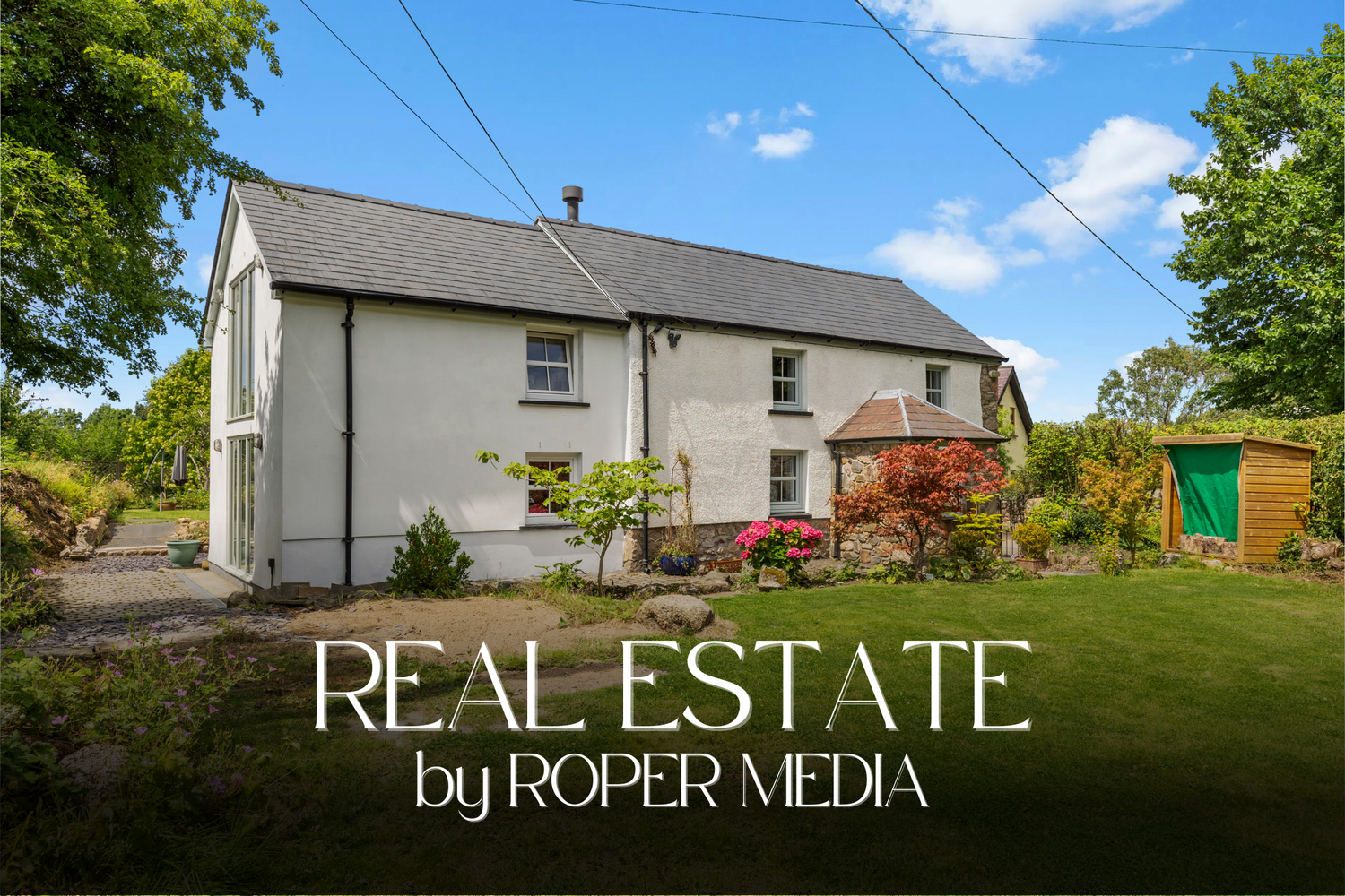 White countryside cottage with large garden and red car parked outside under blue sky with utility lines.