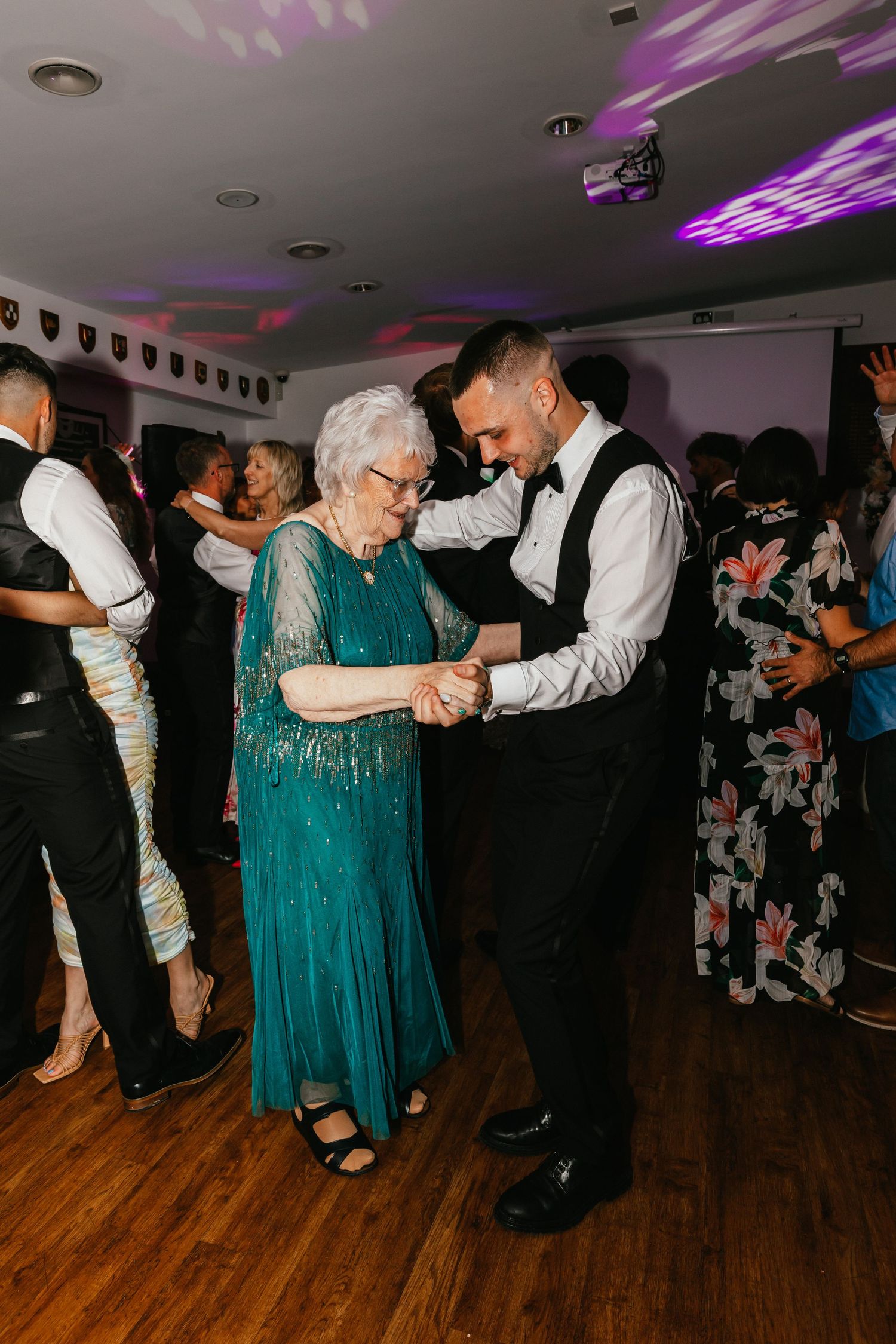 A sweet moment between guests dancing at a reception under purple lighting.