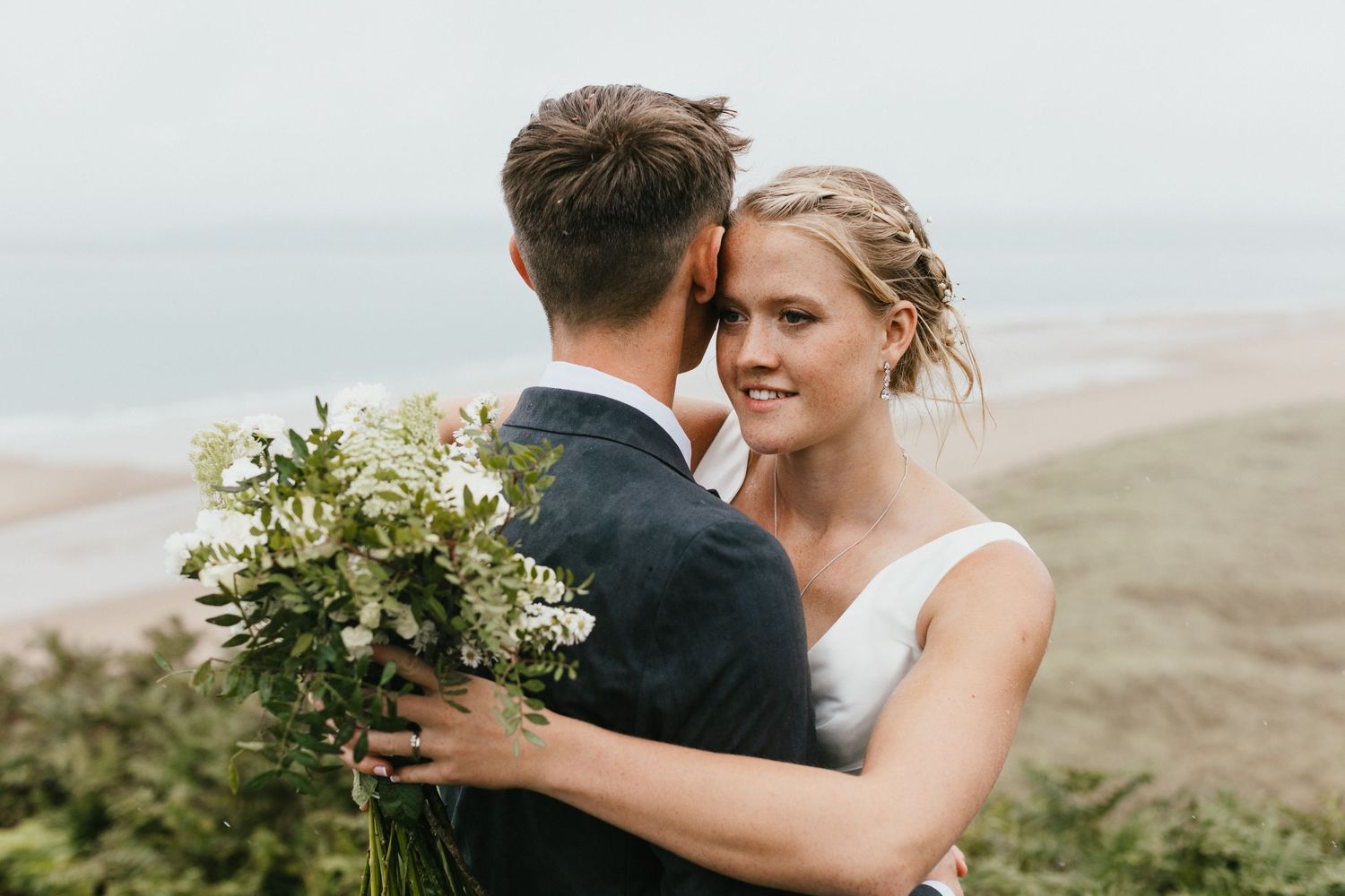 A romantic wedding portrait captured on a hillside with a bouquet of white flowers.