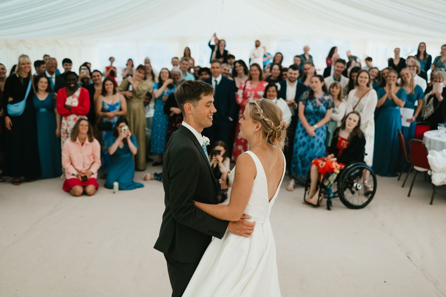 Couple sharing their first dance surrounded by wedding guests in a white reception tent.