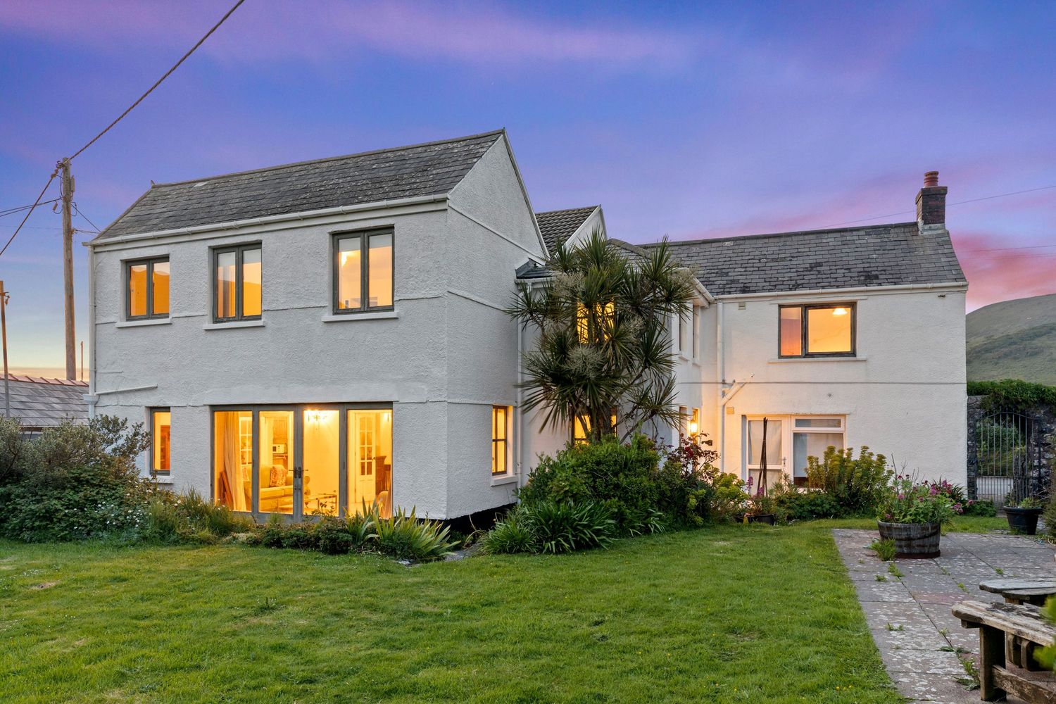 White residential property with illuminated windows and landscaped garden at dusk.