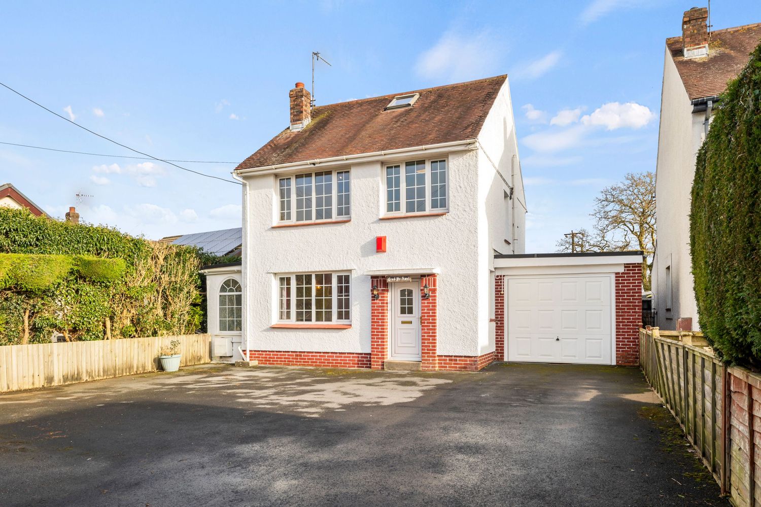 White detached house with red trim and attached garage featuring a spacious driveway.