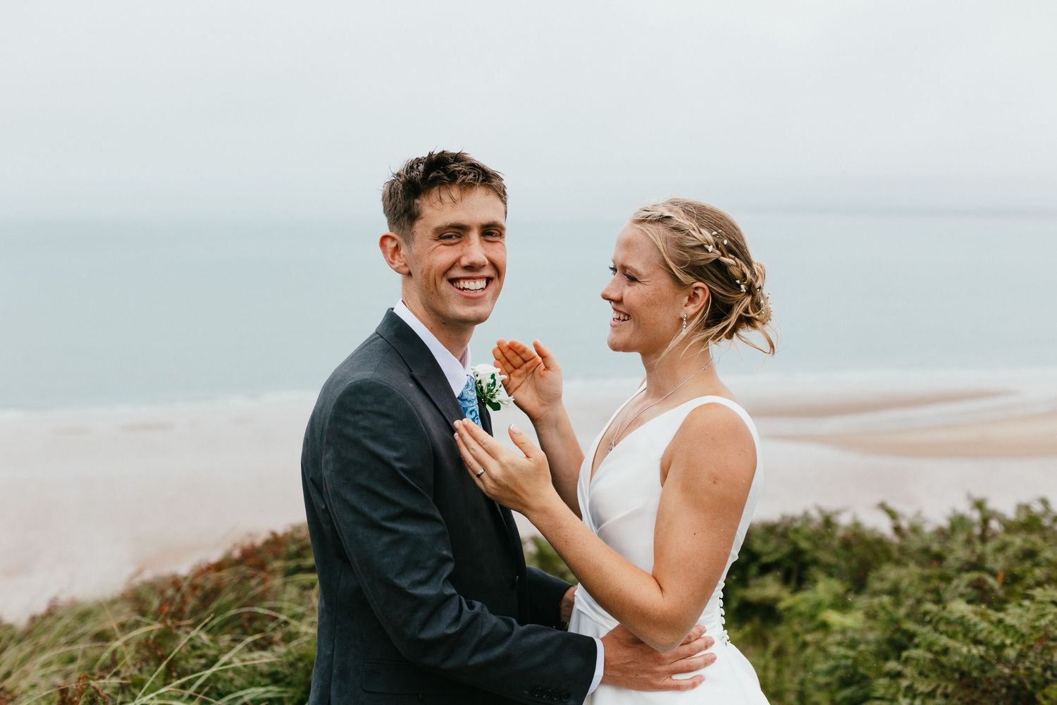 Joyful wedding couple sharing a moment on a coastal clifftop overlooking the ocean.