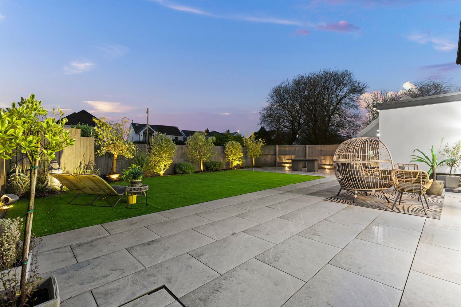 Spacious backyard garden with stone paving and outdoor furniture at twilight.