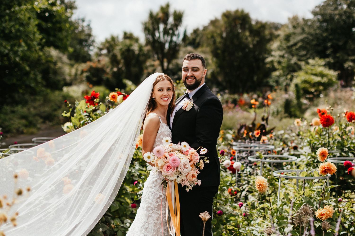 A joyful moment in a garden with colorful flowers and a flowing veil caught in the breeze.