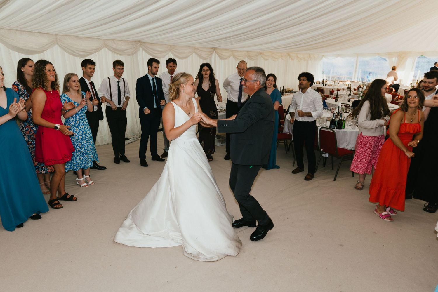 Couple dancing with guests at their wedding reception inside elegant white tent venue.