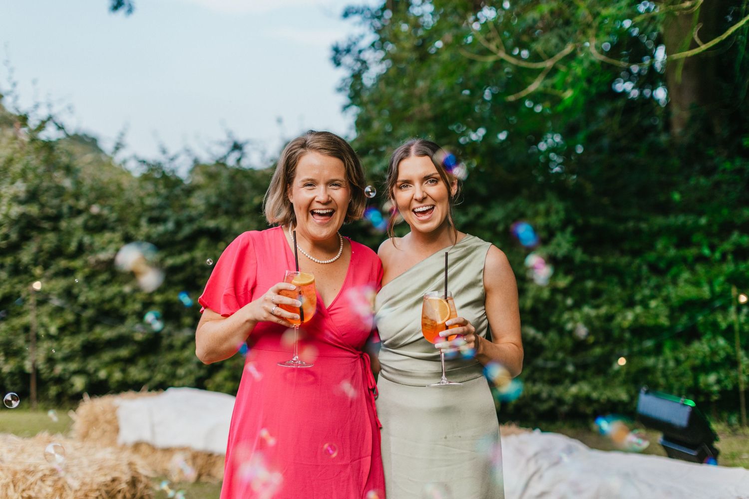 Two wedding guests enjoy drinks outdoors on sunny day.