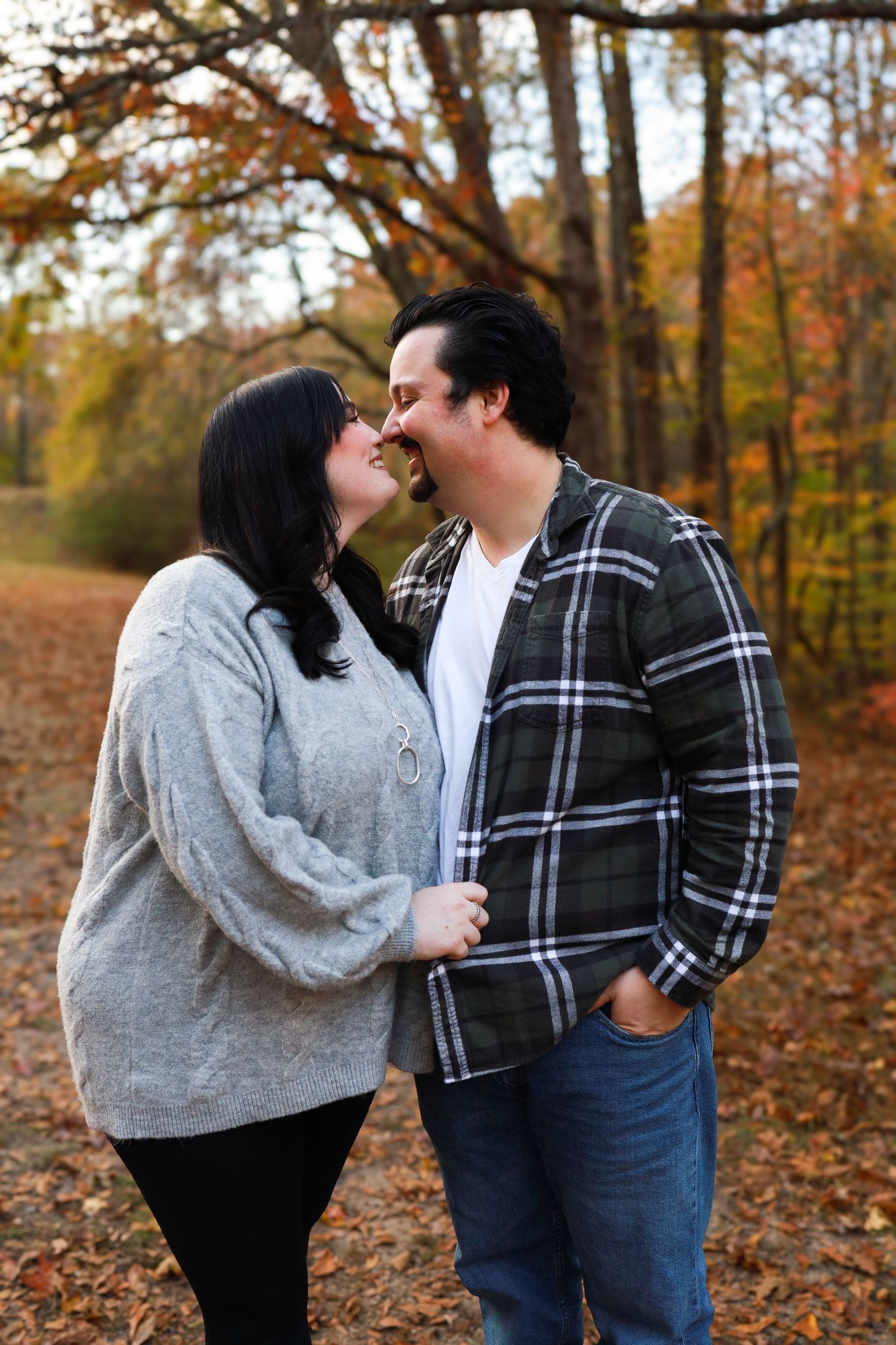 Couple sharing a romantic nose-to-nose moment on a colorful autumn forest path.