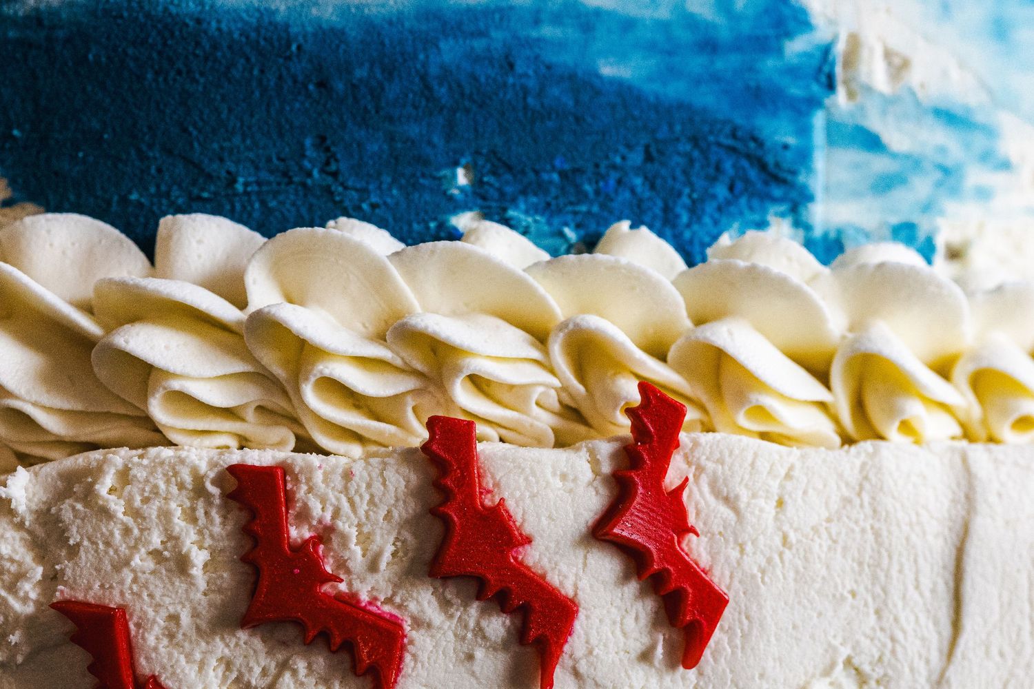 White buttercream frosting with red decorative elements creates an elegant pattern along the edge of a cake.