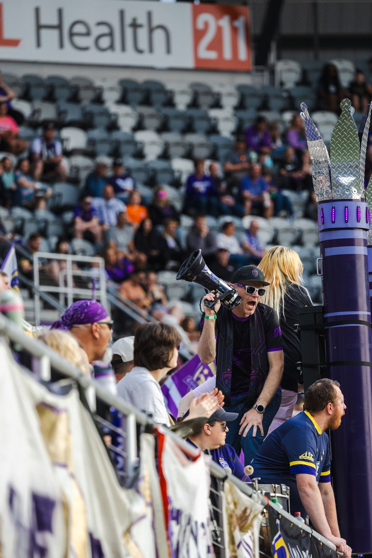 Fans cheering in stadium stands with purple decorative crown visible.