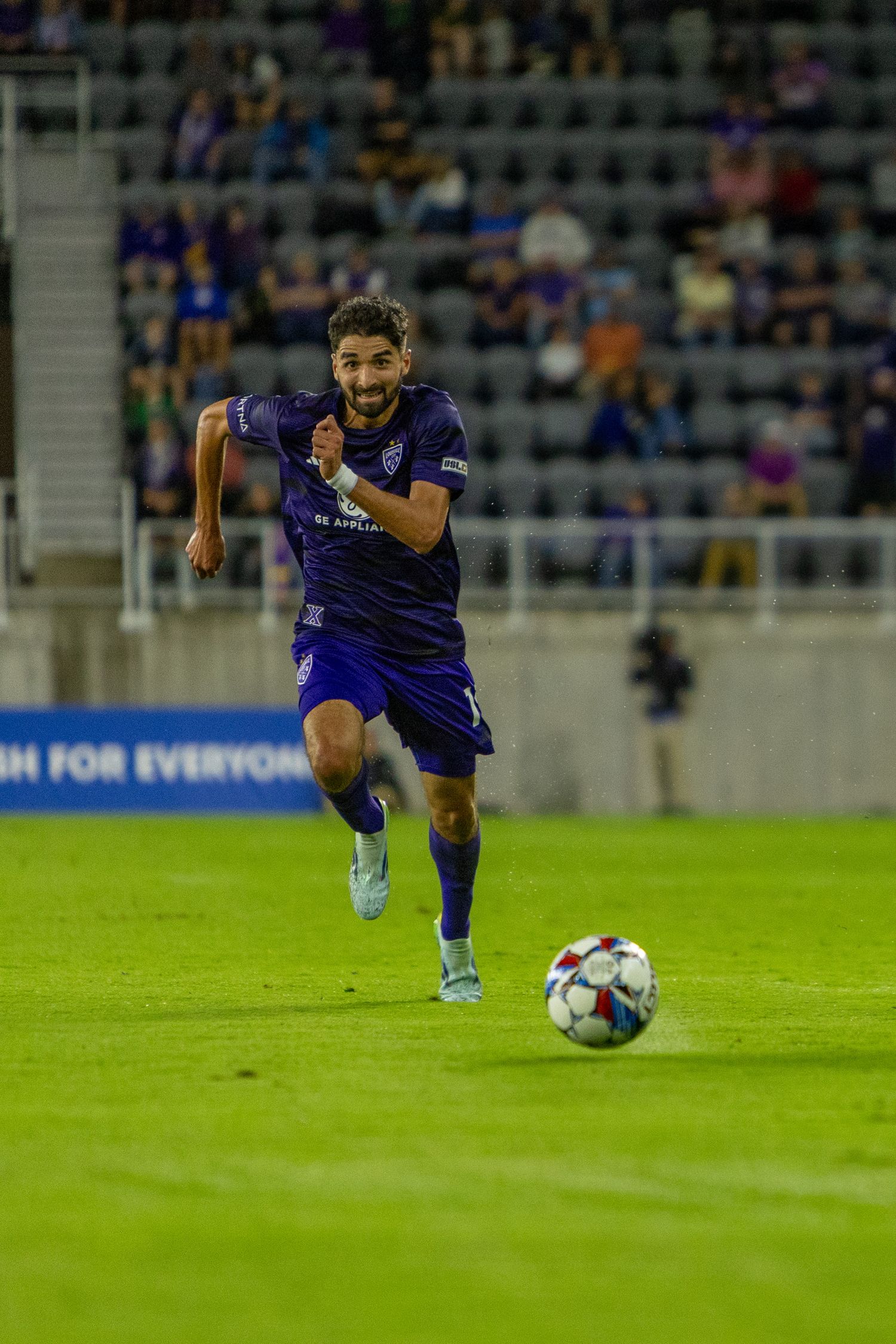 Soccer player in purple jersey dribbling ball down field during match.